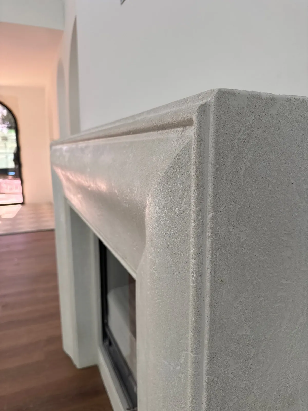Close-up of a white concrete fireplace surround with a curved, stepped mantel profile